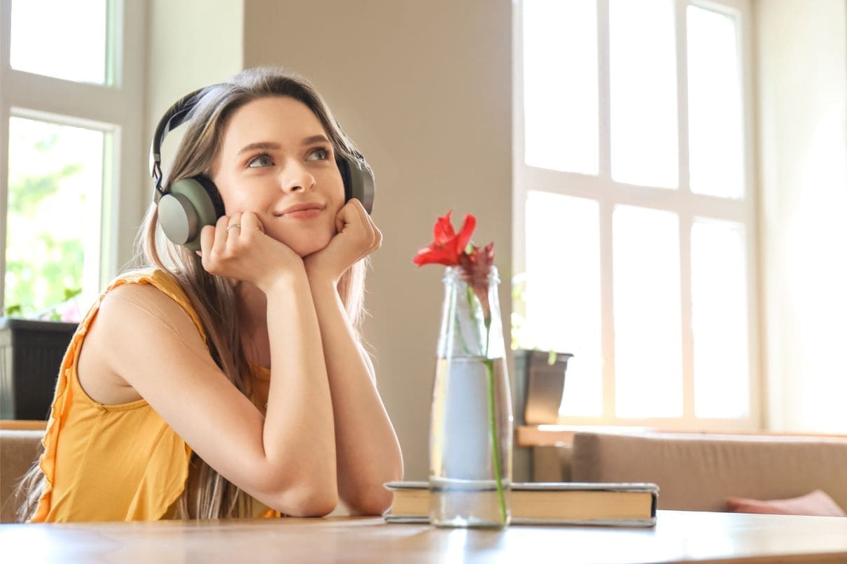 A woman with headphones immersed in her own world, sitting at a table with a book and a vase